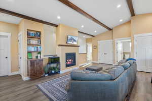 Living room with lofted ceiling with beams, baseboards, wood finished floors, and a glass covered fireplace