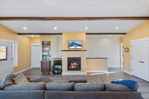 Living area with beamed ceiling, baseboards, a glass covered fireplace, and wood finished floors