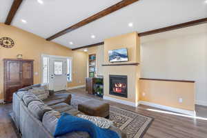 Living area featuring wood finished floors, baseboards, lofted ceiling with beams, recessed lighting, and a glass covered fireplace