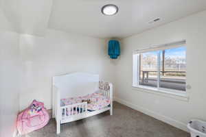 Bedroom with a nursery area, visible vents, baseboards, and carpet