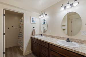 Full bath with double vanity, wood finished floors, baseboards, and a sink
