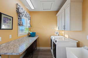 Clothes washing area featuring dark wood-style floors, baseboards, washing machine and clothes dryer, cabinet space, and a sink