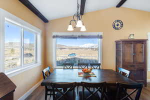Dining room featuring lofted ceiling with beams, baseboards, dark wood-type flooring, and a chandelier