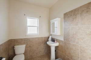 Bathroom featuring toilet, tile walls, and wainscoting