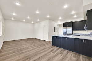 Kitchen featuring dark cabinets, a peninsula, light stone counters, stainless steel fridge, and light wood-type flooring