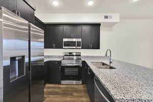 Kitchen featuring appliances with stainless steel finishes, light stone counters, a peninsula, dark wood finished floors, and a textured ceiling
