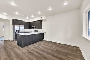 Kitchen featuring a peninsula, stainless steel appliances, light stone countertops, dark wood-style flooring, and recessed lighting