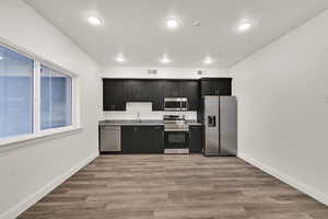 Kitchen featuring stainless steel appliances, light wood-style flooring, dark cabinetry, and light stone countertops