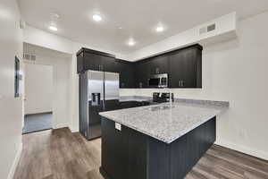 Kitchen featuring stainless steel appliances, light stone countertops, a peninsula, dark wood-style flooring, and a textured ceiling