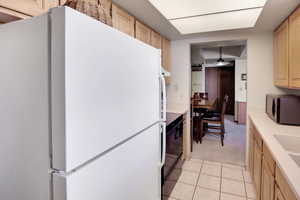 Kitchen with light brown cabinetry, light countertops, freestanding refrigerator, and black microwave