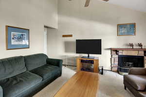 Living room featuring high vaulted ceiling, a ceiling fan, a stone fireplace, and carpet flooring