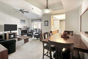 Dining area with visible vents, a ceiling fan, a stone fireplace, light colored carpet, and vaulted ceiling