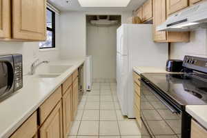 Kitchen with light brown cabinetry, black electric range oven, under cabinet range hood, and a sink