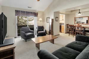 Living area featuring vaulted ceiling, visible vents, and light carpet