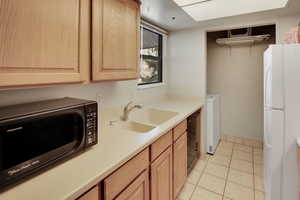 Kitchen featuring a sink, dishwasher, light brown cabinets, and freestanding refrigerator