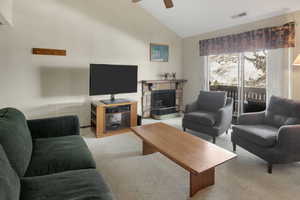 Living room with radiator, visible vents, carpet floors, ceiling fan, and a stone fireplace