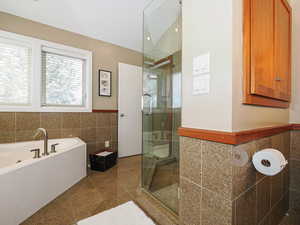Bathroom with a garden tub, granite finish floor, a shower stall, and tile walls