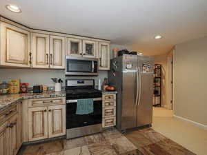 Kitchen with glass insert cabinets, baseboards, recessed lighting, cream cabinetry, and stainless steel appliances