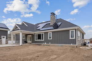 Back of house with roof mounted solar panels, board and batten siding, a chimney, and roof with shingles