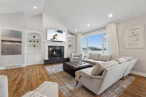 Living room featuring built in shelves, wood finished floors, visible vents, baseboards, and a fireplace