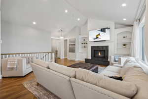 Living room with built in features, a premium fireplace, recessed lighting, wood finished floors, and high vaulted ceiling