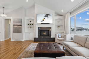 Living area with a high end fireplace, visible vents, built in shelves, baseboards, and wood finished floors