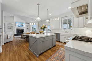 Kitchen with gray cabinetry, open floor plan, dishwasher, lofted ceiling, and a warm lit fireplace