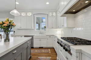 Kitchen featuring dark wood finished floors, custom range hood, gray cabinets, appliances with stainless steel finishes, and a sink