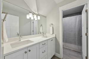 Bathroom featuring double vanity, wood finished floors, lofted ceiling, and a sink