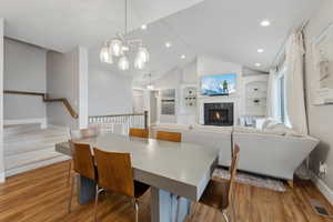 Dining room featuring visible vents, built in features, wood finished floors, a lit fireplace, and lofted ceiling