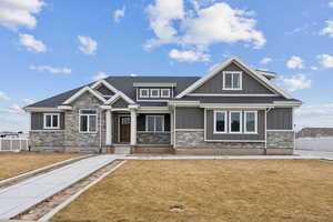 Craftsman-style home featuring stone siding, board and batten siding, a front lawn, and fence