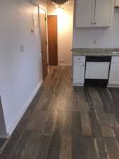 Kitchen with white cabinetry, dark wood-type flooring, baseboards, and white dishwasher