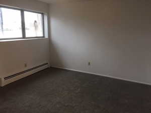 Spare room with dark colored carpet, a baseboard heating unit, and baseboards