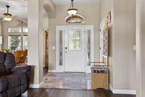 Entrance foyer featuring arched walkways, baseboards, a ceiling fan, and wood finished floors