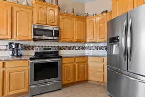 Kitchen with light stone counters, stainless steel appliances, and decorative backsplash