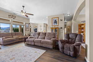 Living room with visible vents, arched walkways, dark wood finished floors, and a ceiling fan