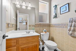 Half bath with tile walls, a wainscoted wall, toilet, and vanity