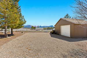 View of yard featuring a detached garage, fence, driveway, an outdoor structure, and a mountain view