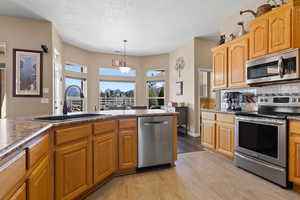 Kitchen featuring a sink, decorative backsplash, appliances with stainless steel finishes, dark countertops, and decorative light fixtures