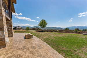 View of grassy yard featuring an outdoor fire pit, a patio area, and a mountain view