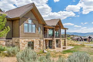 Back of house featuring a balcony, stone siding, a patio, and a mountain view