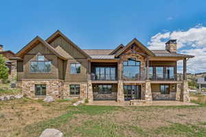 Rear view of house with stone siding, a standing seam roof, a patio, a chimney, and a metal roof