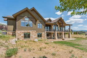 Rear view of property with a balcony, a patio area, stone siding, and board and batten siding