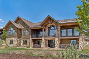 Back of property featuring stone siding, a balcony, a standing seam roof, board and batten siding, and a metal roof