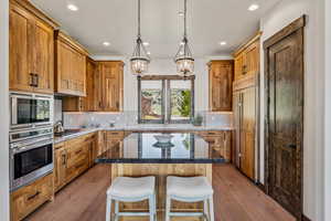 Kitchen featuring built in appliances, a chandelier, recessed lighting, dark stone countertops, and a kitchen breakfast bar