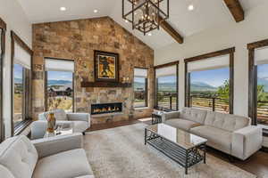 Living room with a stone fireplace, wood finished floors, a chandelier, recessed lighting, and beam ceiling