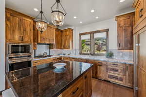Kitchen featuring stainless steel appliances, a chandelier, decorative backsplash, brown cabinetry, and recessed lighting