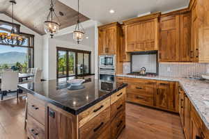 Kitchen with appliances with stainless steel finishes, a chandelier, wood-type flooring, vaulted ceiling, and decorative backsplash
