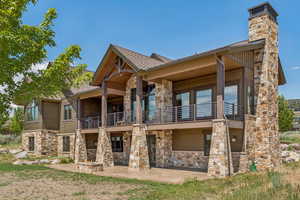 Back of property with a balcony, stone siding, a patio, and a chimney