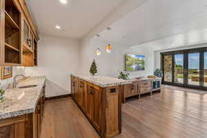 Kitchen featuring brown cabinetry, a peninsula, open shelves, light stone counters, and hardwood / wood-style flooring